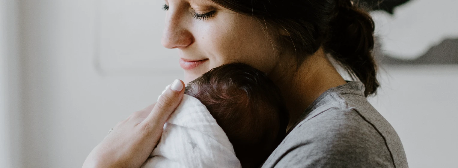 Photograph of a mother cradling a newborn baby in their arms.
